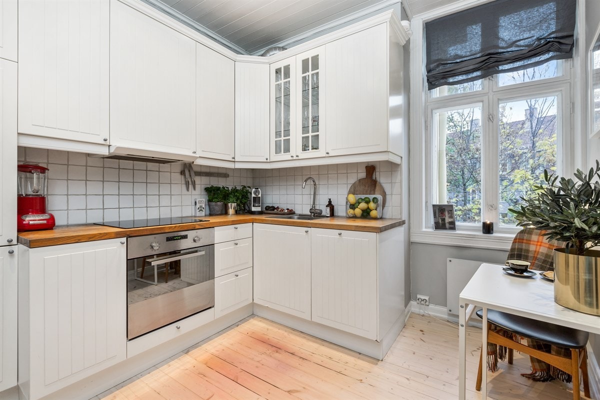 Praktisk og hyggelig kjøkken fra IKEA med malte profilerte fronter, heltre benkeplate, ventilator, fliser på vegg over benk og integrerte hvitevarer: komfyr, keramisk topp, oppvaskmaskin, kjøl-og fryseskap. Galleribilde
