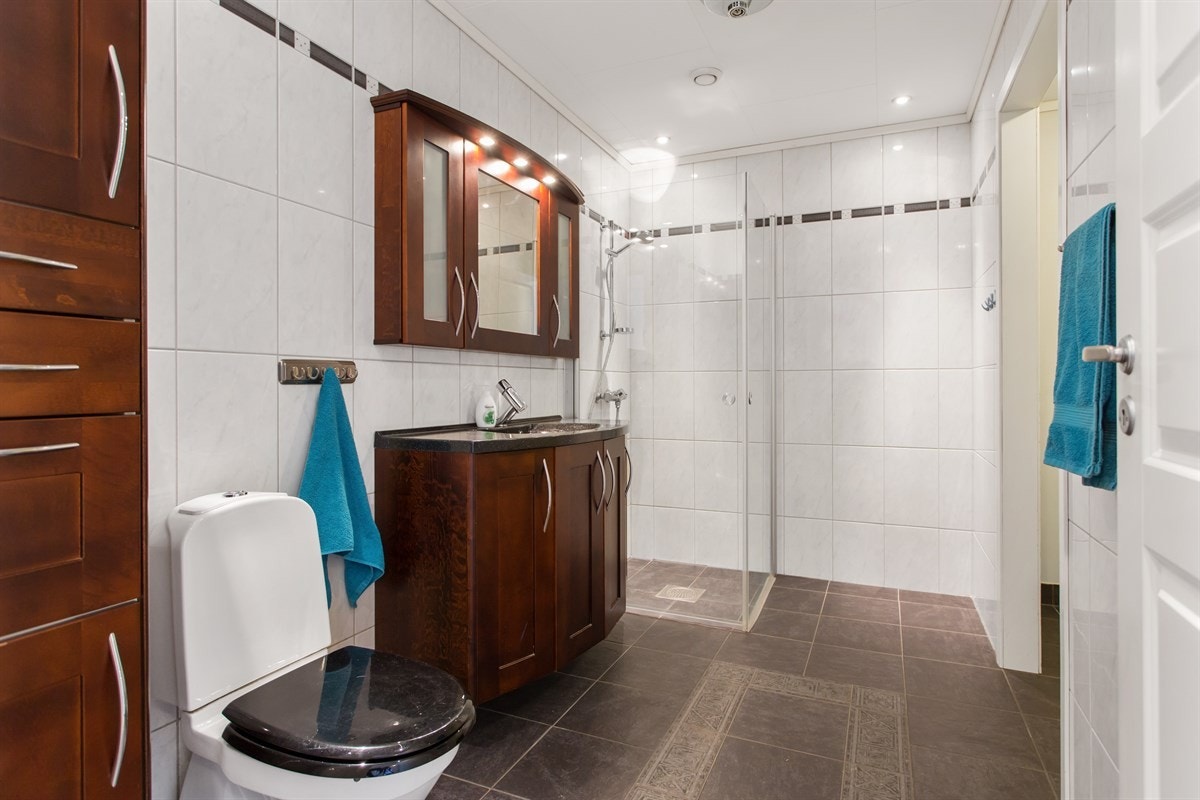 Badet i første etasje er helfliset og innredet med klassiske baderomsmøbler i samme stil som kjøkkenet, toalett og dusjhjørne. I tillegg har det blitt laget plass til en vaskerom-nisje der vasking og oppbevaring av tøy kan skje på en effektiv måte. Galleribilde