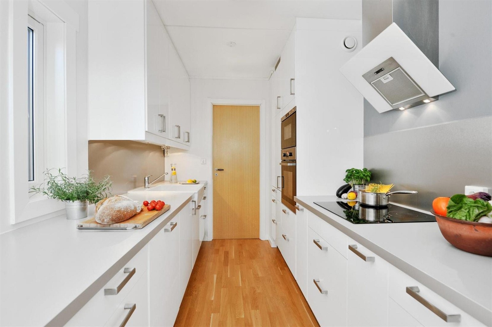 Moderne kjøkkeninnredning i hvit høyglans med integrerte hvitevarer. Inngang fra kjøkkenet til praktisk vaskerom Galleribilde