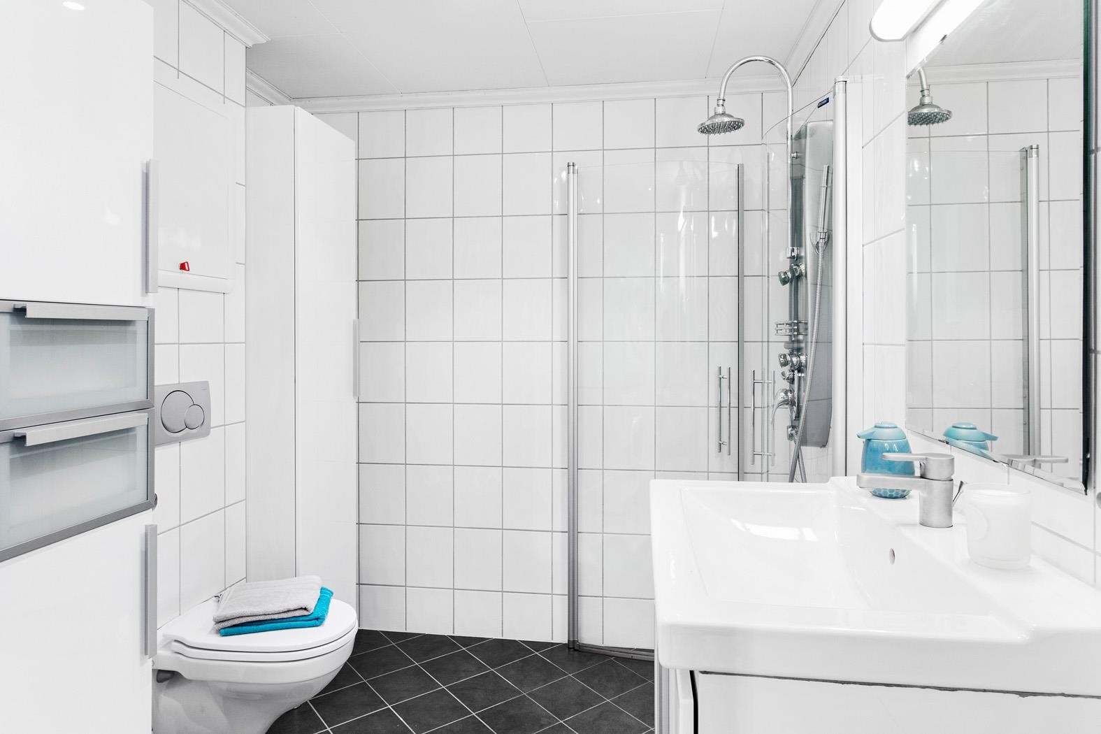 Pent helfliset bad som inneholder servantmøbel, speilskap, vegghengt toalett, dusjhjørne og høyskap. Her er det opplegg for vaskemaskin. Galleribilde