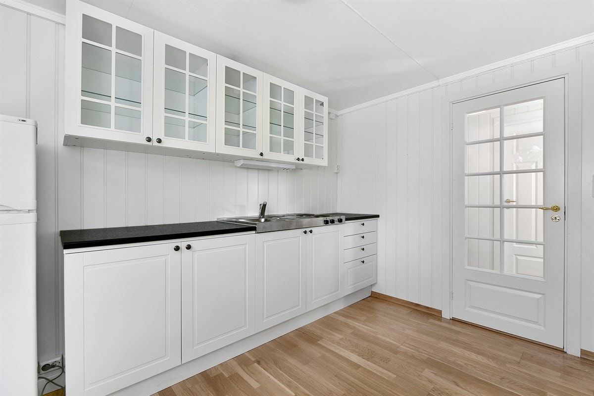 Kjøkkenet i utleiedelen har en innredning med profilerte fronter og vitrineskap. Videre er det benkebelysning, laminert benkeplate, enkel vaskekum og kombinert kjøl/frys Galleribilde