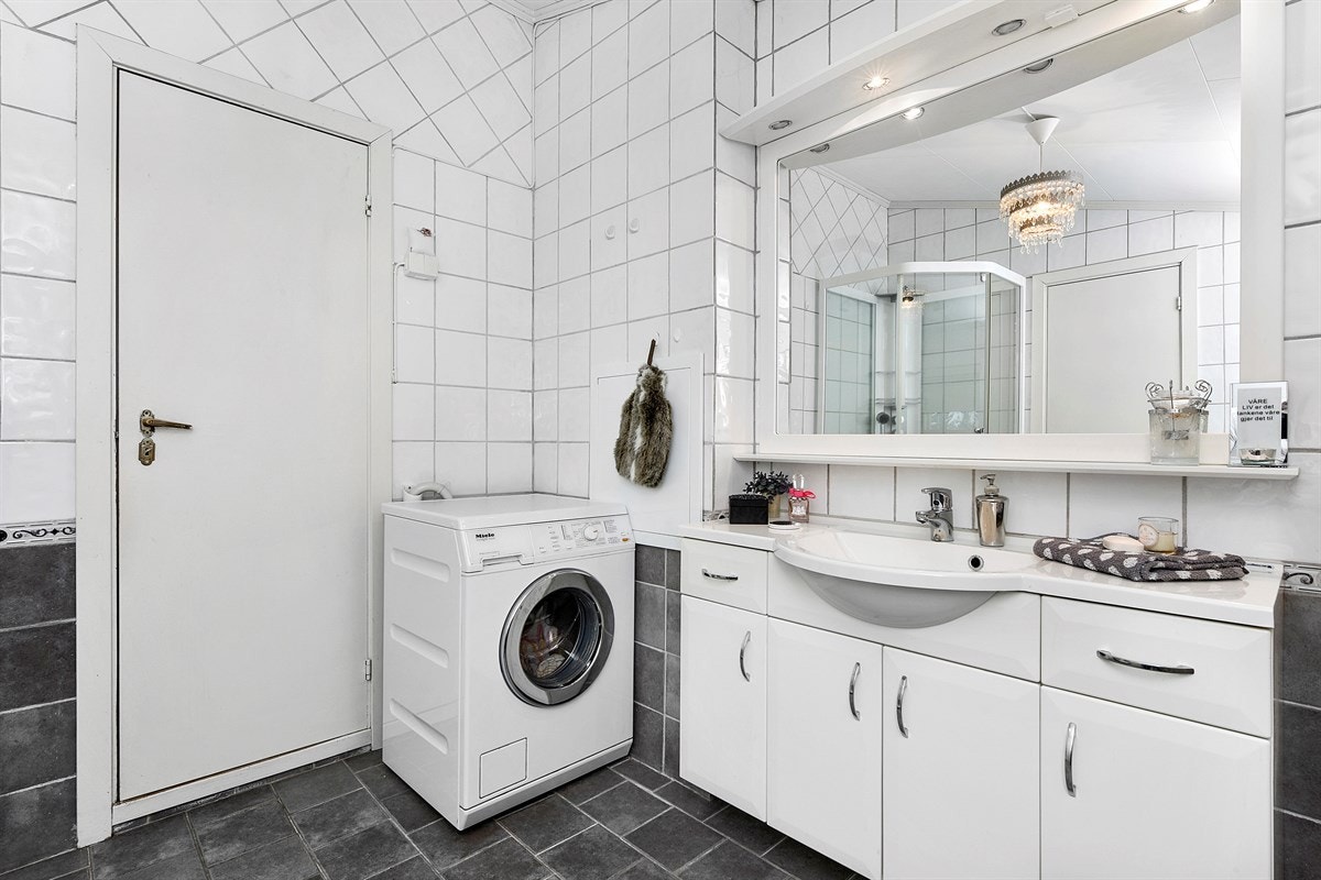 Badet er utstyrt med fliser, gulvvarme, en lys baderomsinnredning bestående av speil med hylle og overbelysning, samt servantskap og tilhørende høyskap. Galleribilde