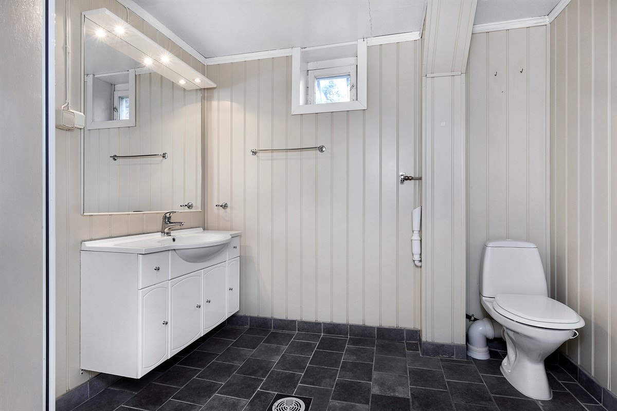 Rommet har speil med overbelysning, servantmøblement med profilerte fronter, frittstående toalett og dusjkabinett. Det er også opplegg for vaskemaskin på dette badet. Galleribilde