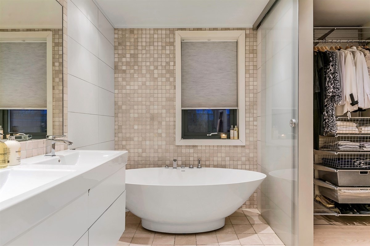 Badet har lekre fliser i fin kombinasjon, et innbydende badekar, samt dusjhjørne med innfellbare glassdører og regnfallsdusj Galleribilde