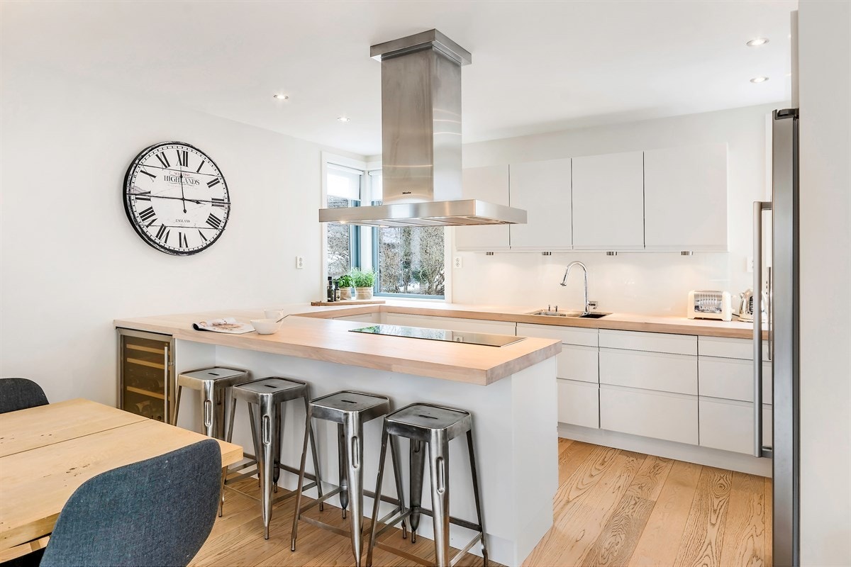 Kjøkkenet ligger i åpen løsning mot stuen, hvor en stilig barløsning bidrar med både oppbevaring, kokesone og sitteplasser Galleribilde