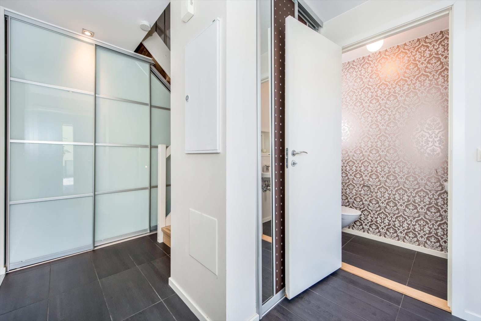 Flislagt entrè med inngang til gjestetoalett. Det er satt opp smarte garderobeløsninger med skyvedører til sko og yttertøy. Galleribilde