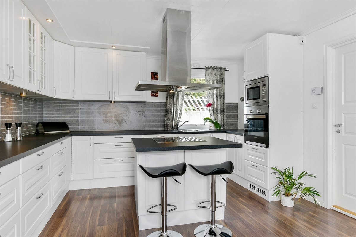 Den takhøye innredningen fra 2013 har hvite, profilerte fronter, vitrineskap, benkebelysning, grå flisplate over benk, og laminert benkeplate med enkel vaskekum. Galleribilde