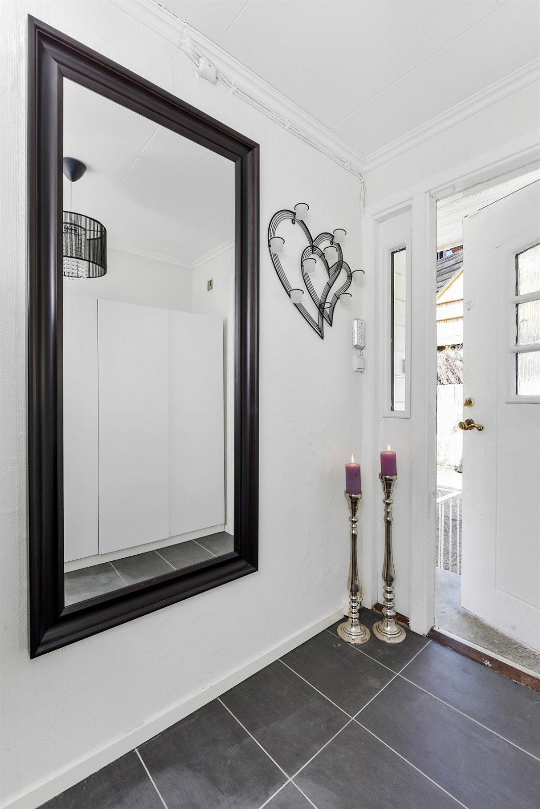 Entreen er lys og innbydende med grå, rektangulære fliser på gulv, hvitmalte vegger og listverk, samt et praktisk garderobeskap med god plass for oppbevaring av ytterklær. Galleribilde