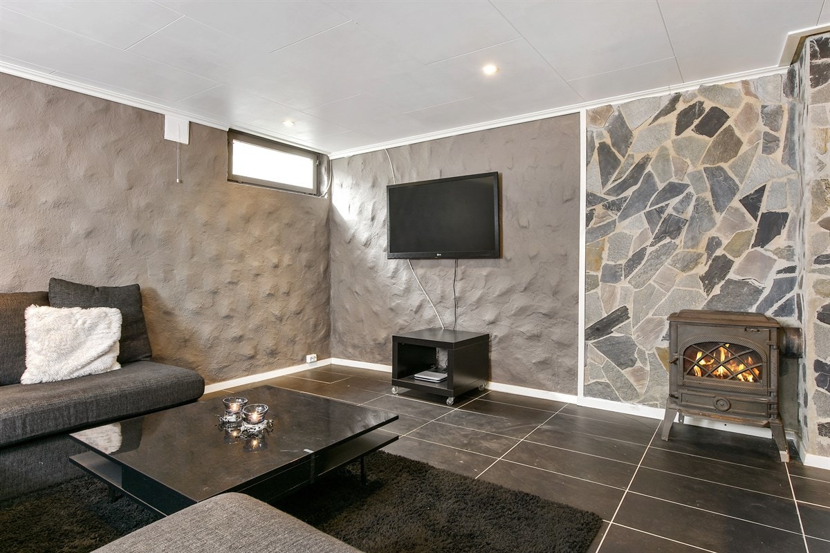 Rommet gulvvarme, downlights, og integrert spotbelysning i vegg i trappeløp. Videre er det plassert en effektiv vedovn ved pipeløp og brannvegg kledd i naturstein, samt en stilfull, vegghenget el-peis på motsatt vegg. Galleribilde
