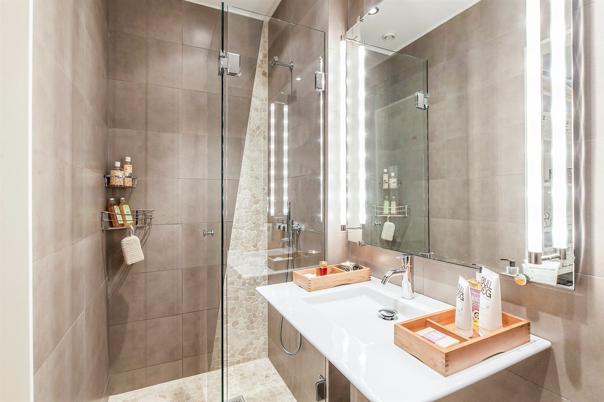 Dusjplass med skjermende glassvegg og servant med speil og belysning over. Galleribilde