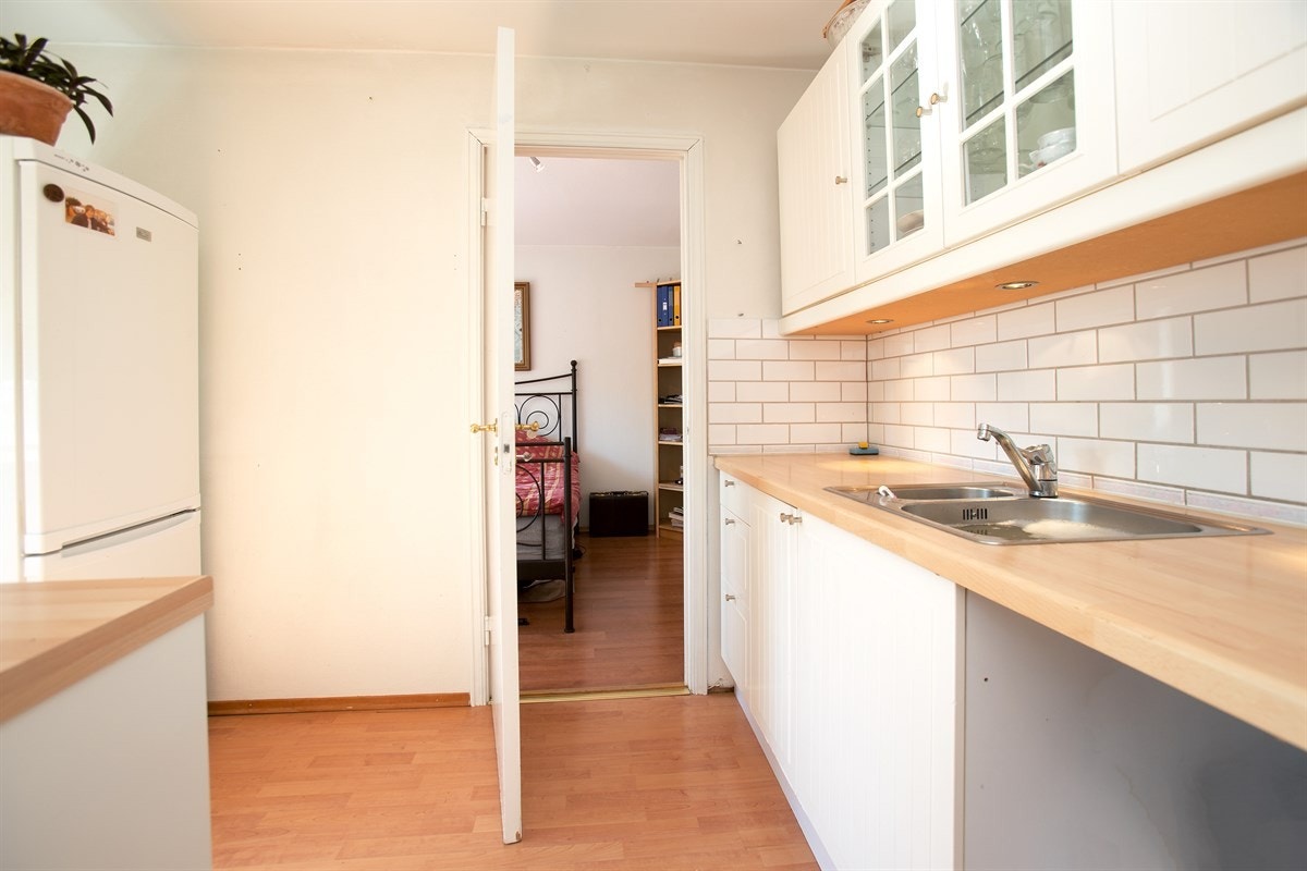 Innredningen har hvite, profilerte fronter, benkebelysning og fliser over en laminat benkeplate med nedfelt vaskekum. Galleribilde