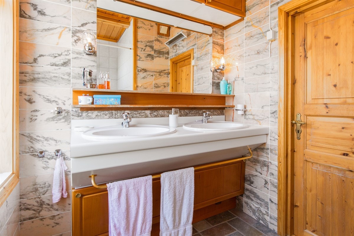 PROA Eiendomsmegling - Ett av boligens bad finner vi vis á vis stuen. Kvalitet var i høysetet da badet ble satt i stand. Her finner man detaljer som Poggenpohl innredning med dobbel vask, skifer på gulv over varme samt fliser i marmor på vegger. Galleribilde