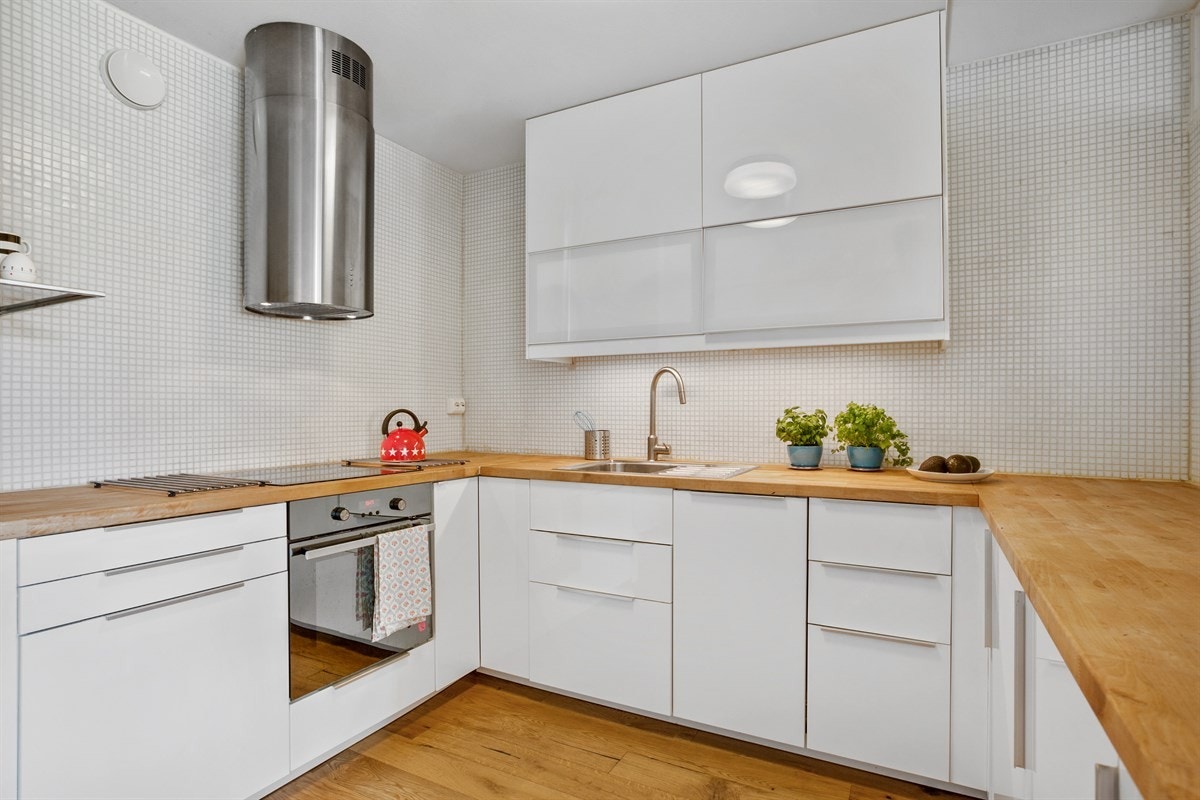 Lys og moderne kjøkkeninnredning med heltre benkeplate. Integrert ovn, koketopp, oppvaskmaskin, fryseskap og kjøleskap. Galleribilde