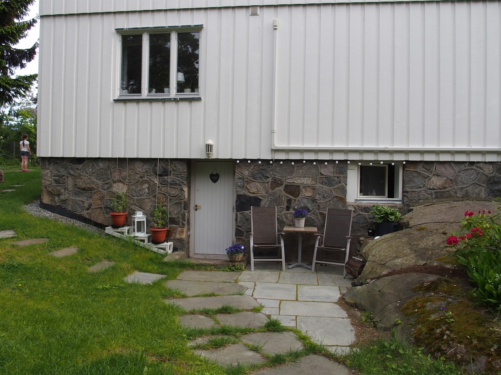 Inngangsparti med uteplass. Kjøkkenvindu til høyre og sov (evt stue) oppe til venstre. Galleribilde