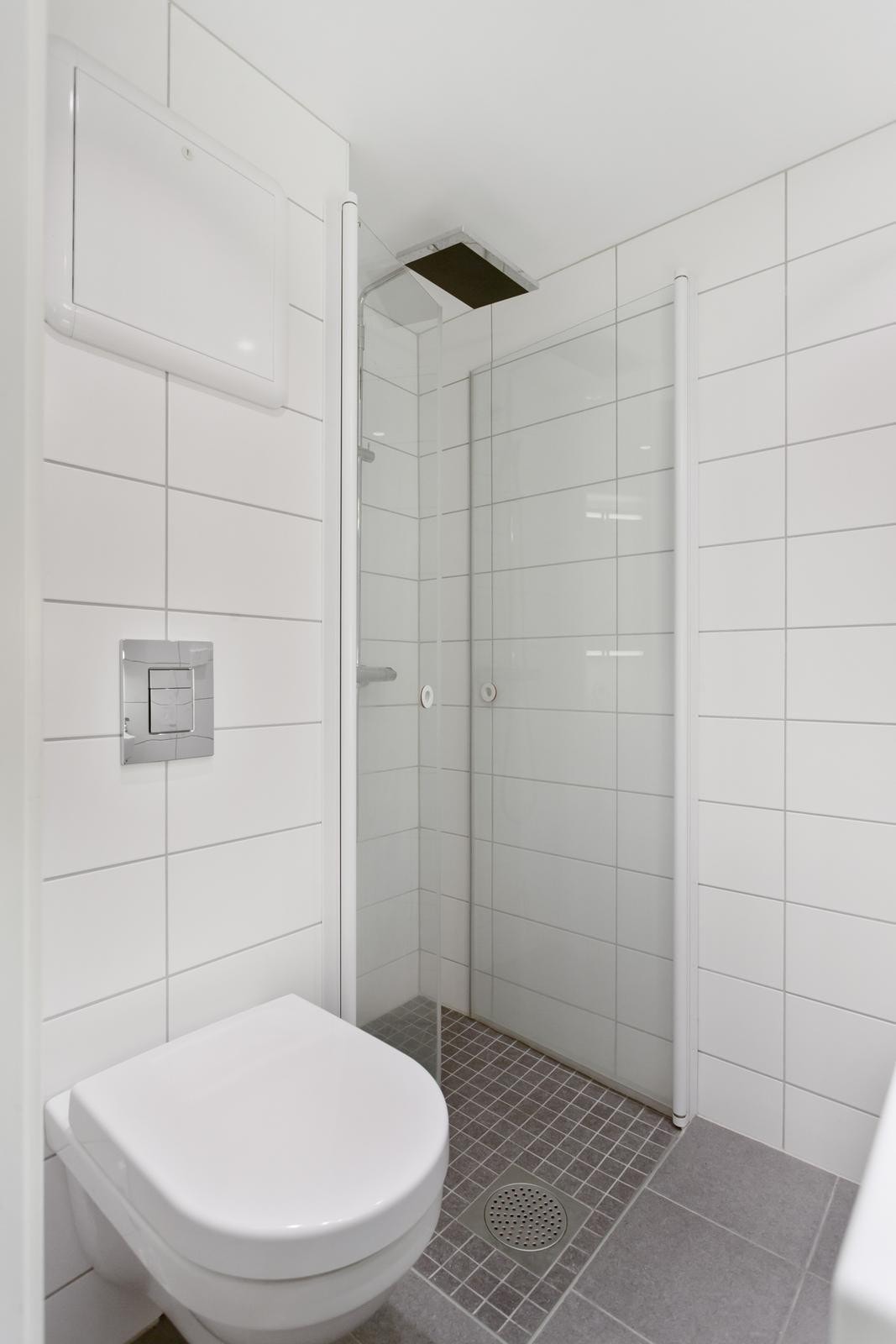 Nytt vegghengt toalett, fliser på vegger og gulv, arealeffektive, innfeldbare dusjvegger og downlights i tak. Galleribilde