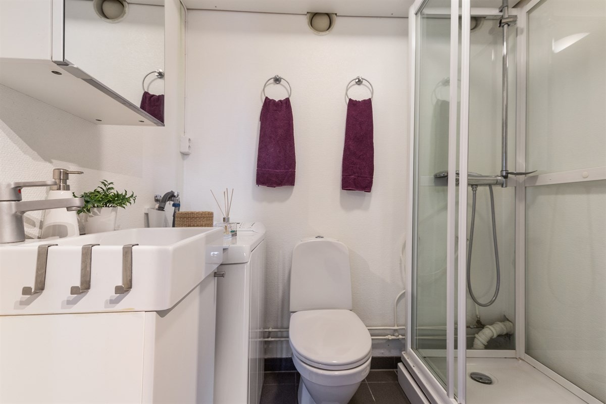 Flislagt bad med opplegg til vaskemaskin. Skap ved siden av kabinett følger Galleribilde