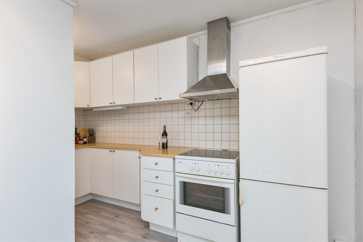 Lys innredning på kjøkken. Komfyr og kjøleskap følger leiligheten Galleribilde