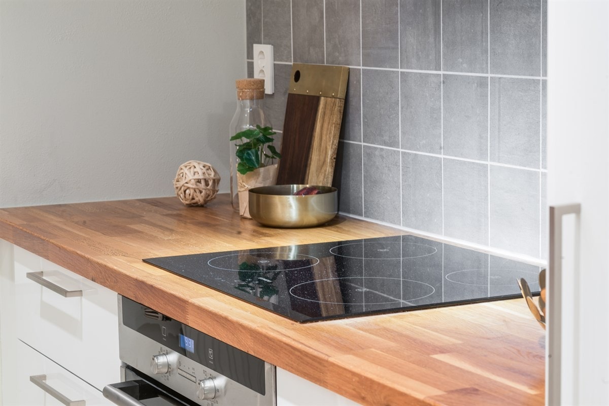 Innredningen har hvite høyglansfronter, benkebelysning, lysegrå fliser over benk, og heltre benkeplate med enkel vaskekum. Galleribilde