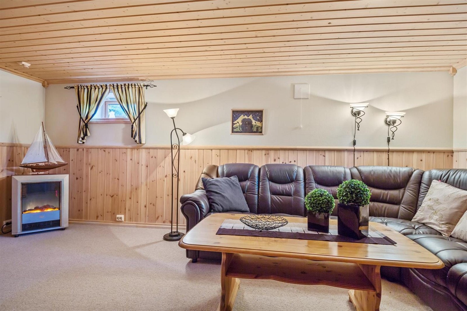 Romslig kjellerstue med teppe på gulv, brystning og malt miljøtapet på vegger og panel i himling. Galleribilde