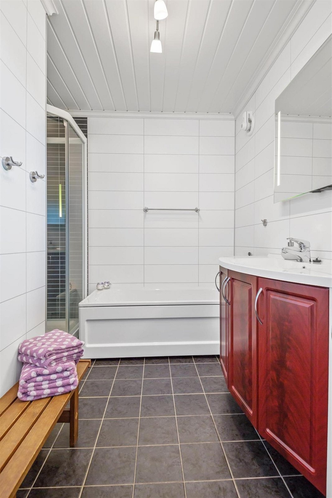 Badet er i vinkel og har både badekar og dusjkabinett, servant i innredning og vegghengt toalett. Galleribilde