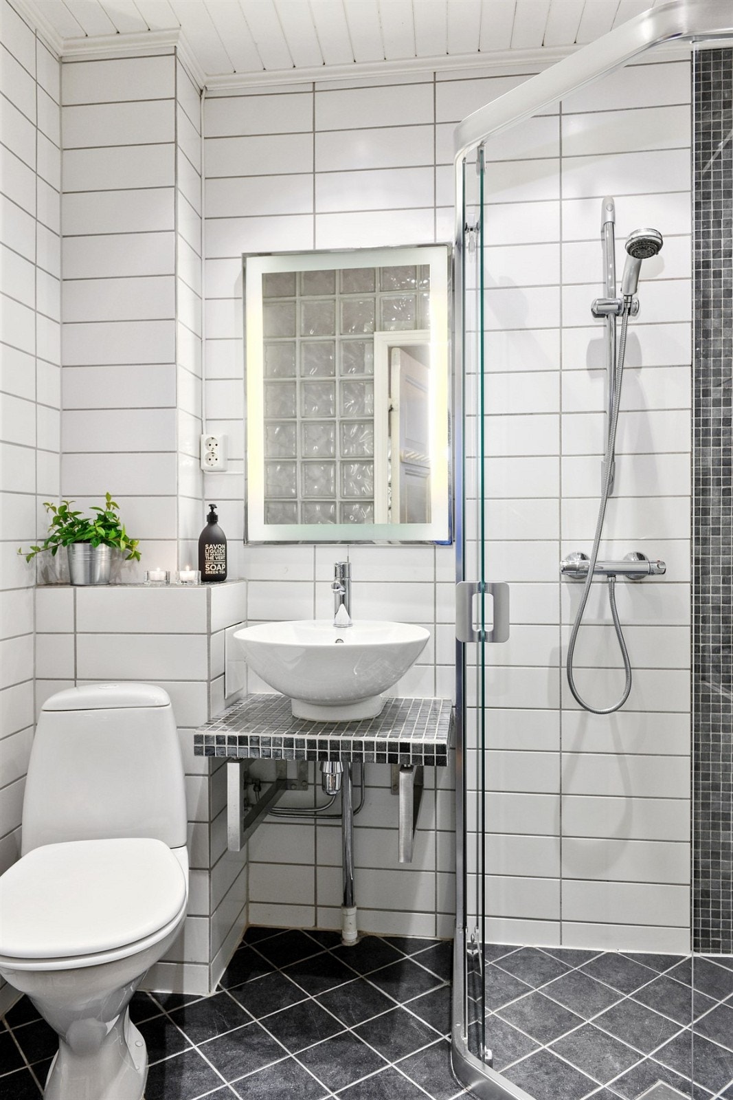 Delikat baderom/wc fra 2005 med servant på benkeplate med mosaikkfliser, toalett og dusj med dusjhjørne i glass. Galleribilde