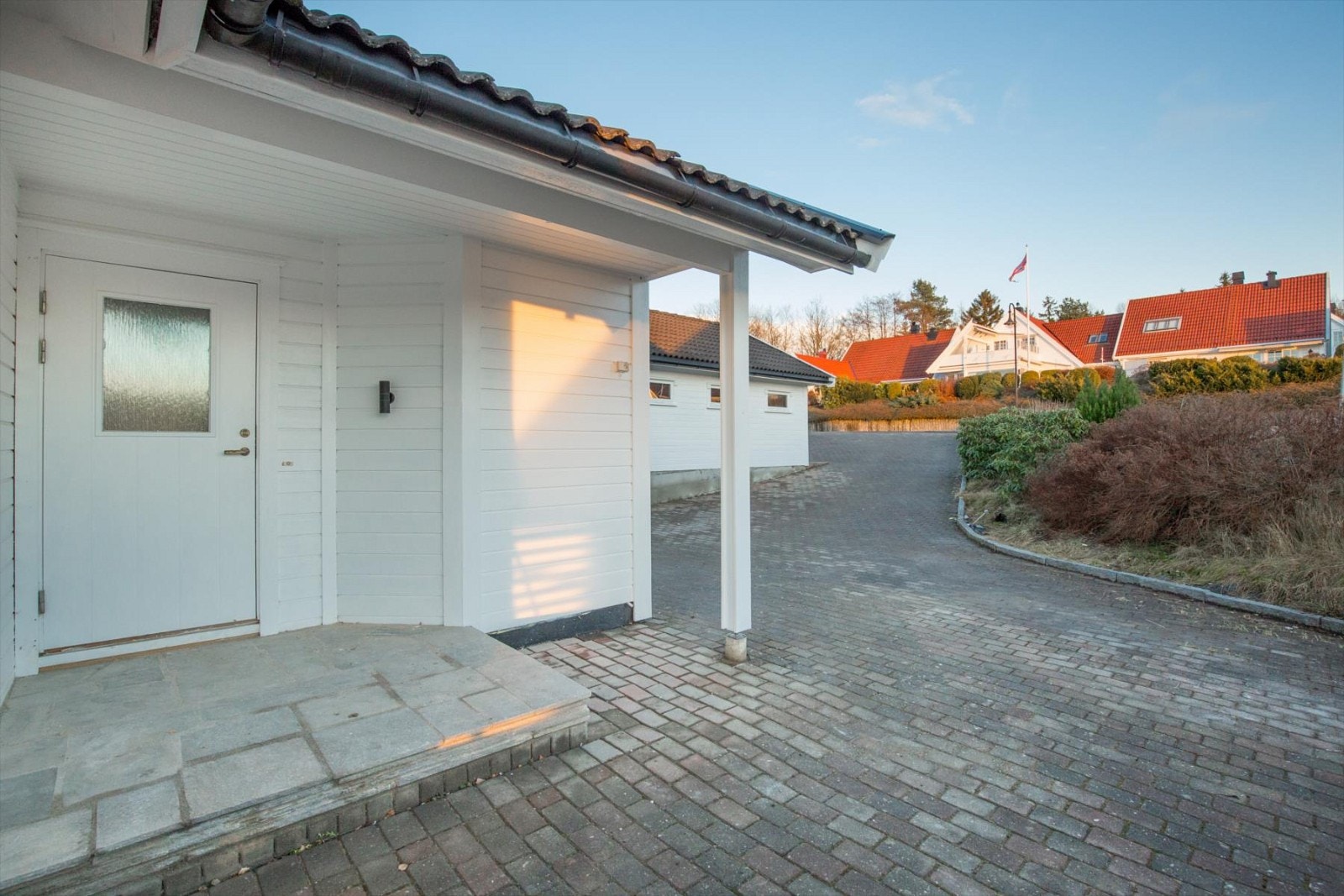 Pent opparbeidet inngangsparti og gårdsplass. I bakgrunnen sees den doble garasjen. Huset er utvendig malt 2016. Galleribilde