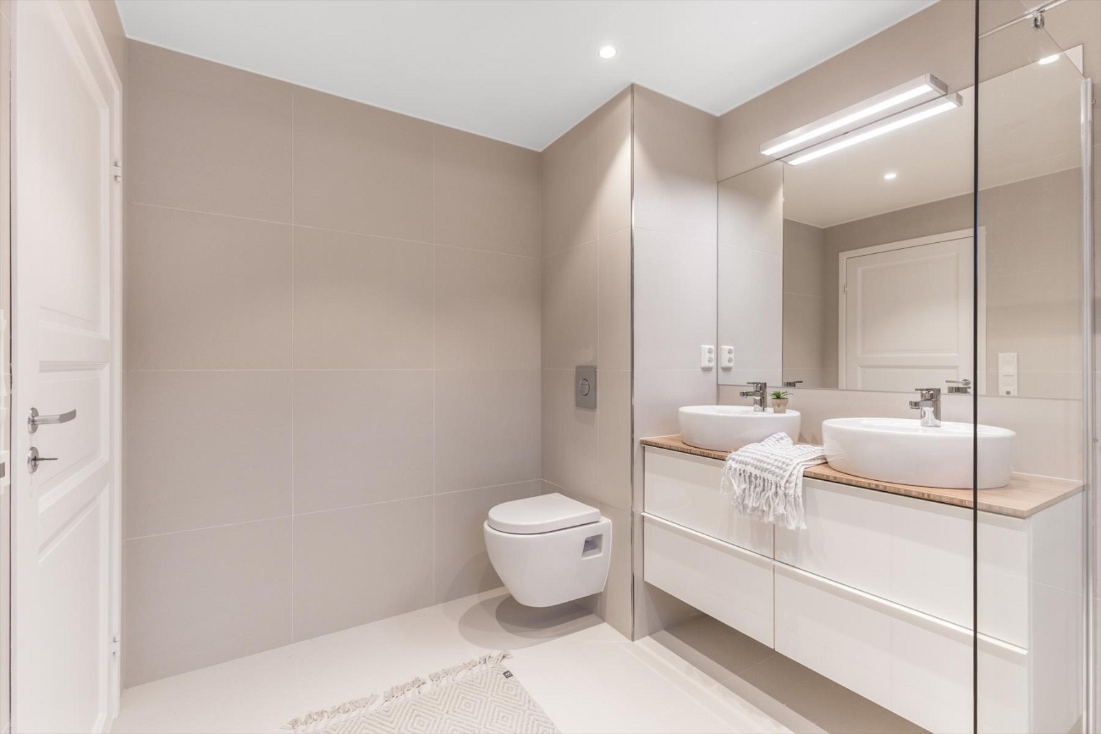 Rommet er innredet med fliser på vegger og gulv med varmekabler og inneholder bl.a. veggmontert toalett, stor dusjnisje med glassdører, servant på baderomsinnredning med underskap og speil. Galleribilde