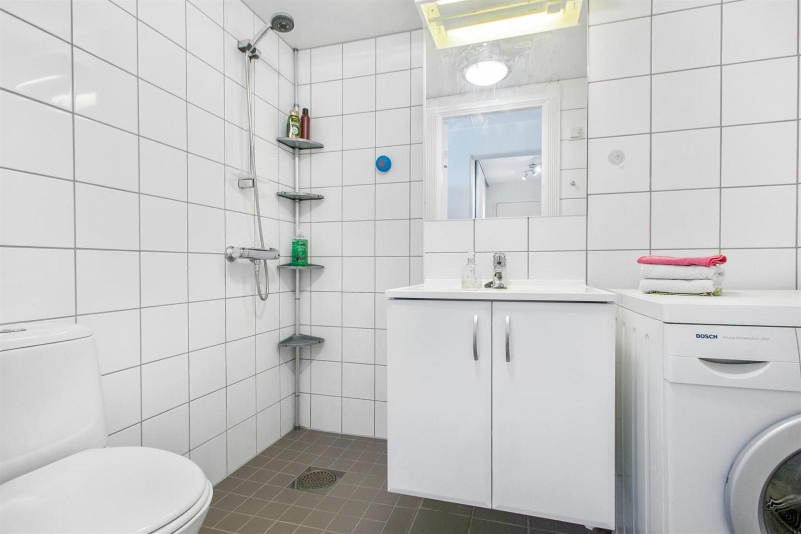 Badet er lyst og flislagt med opplegg for vaskemaskin Galleribilde