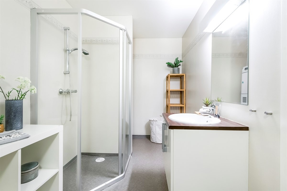 Pent, romslig bad utstyrt med hvit baderomsinnredning, dusjhjørne i glass og toalett. Galleribilde