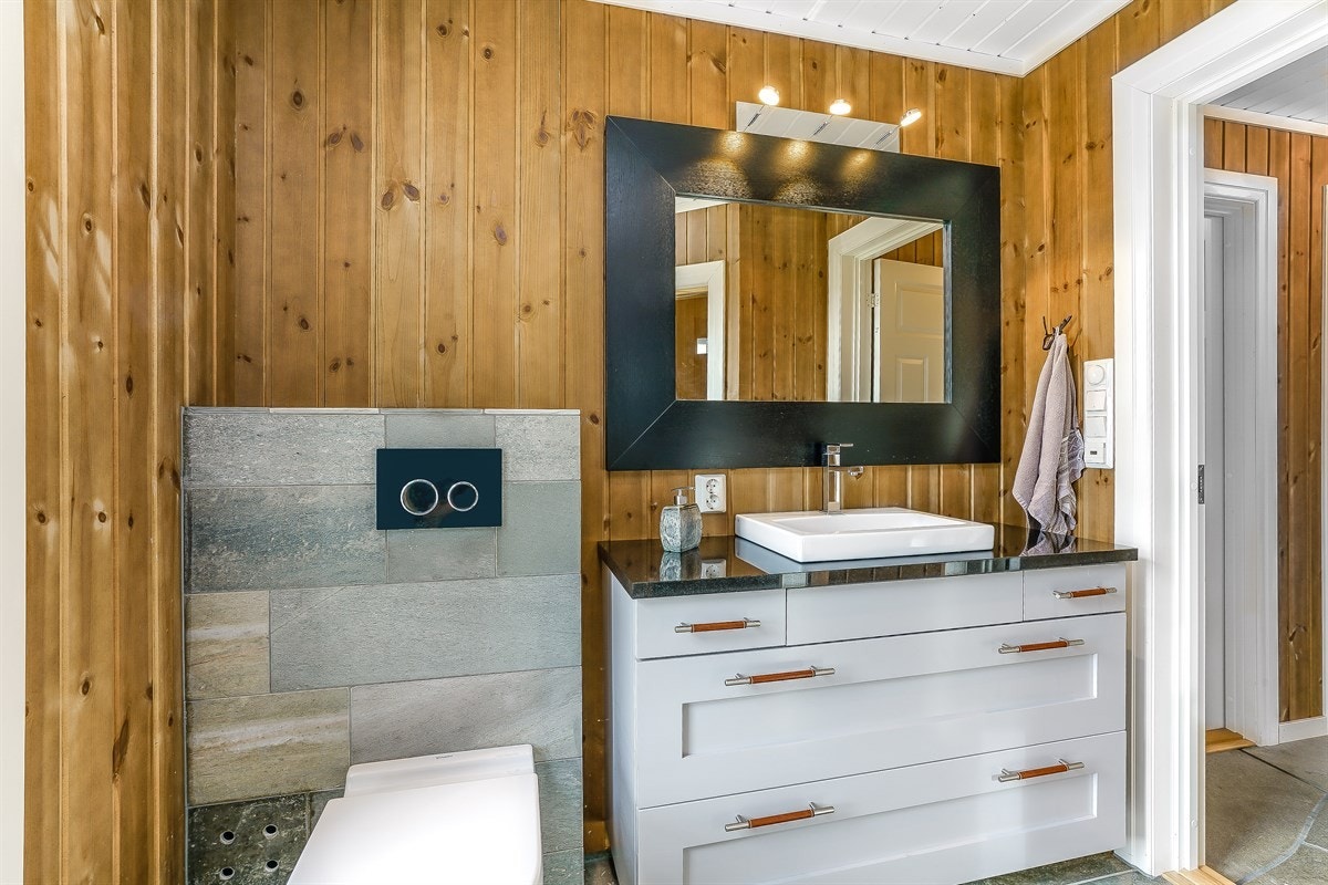 Boligen inneholder et bad og separat vaskerom. Badet er innbydende med lekre detaljer som skiferfliser med lun varme på baderomsgulv, panelte vegger med matchende fliser bak toalett og downlights i hvitmalt himling Galleribilde