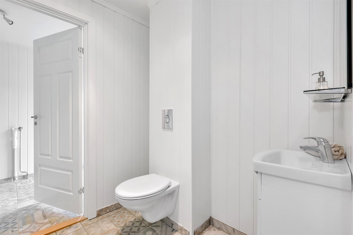 Innenfor det separate toalettrommet har boligen et praktisk vaskerom med stilfulle gulvfliser, malt veggpanel, gulvvarme og godt lysinnslipp fra stort vindu. Galleribilde