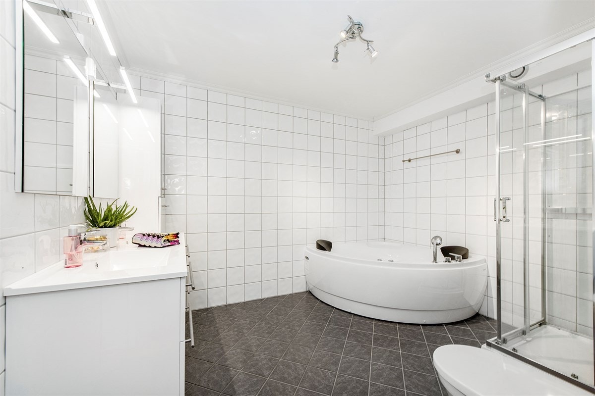 Det romslige badet har mørke gulvfliser, hvite veggfliser og spotlights i himling. Galleribilde