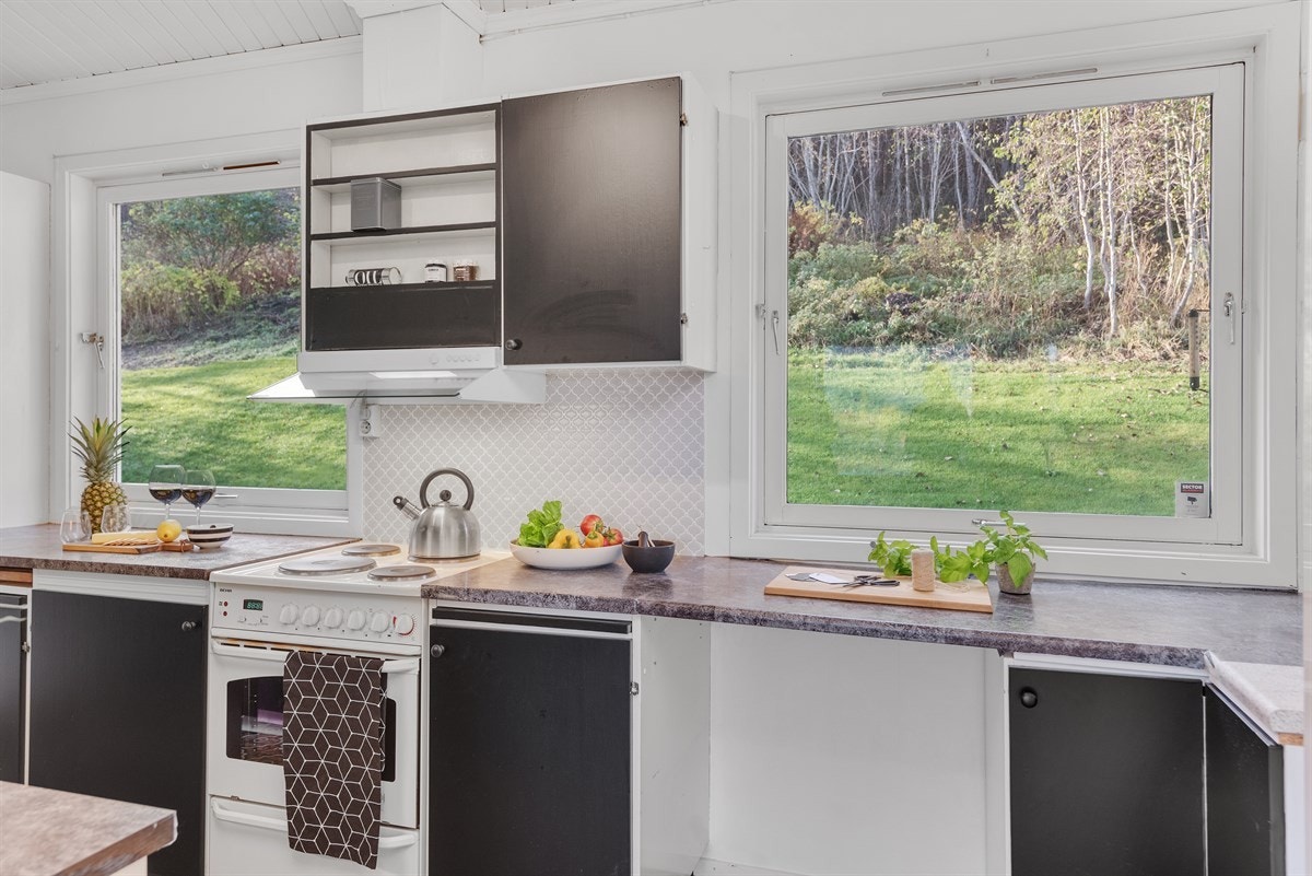 Kjøkkenet har fått et kosmetiskløft nå i 2017, med matte, sorte fronter og lyse vegger og tak. Over kjøkkenbenken har man to store vindu, som sikrer godt med naturlig lys og utsyn mot gårdsplassen Galleribilde