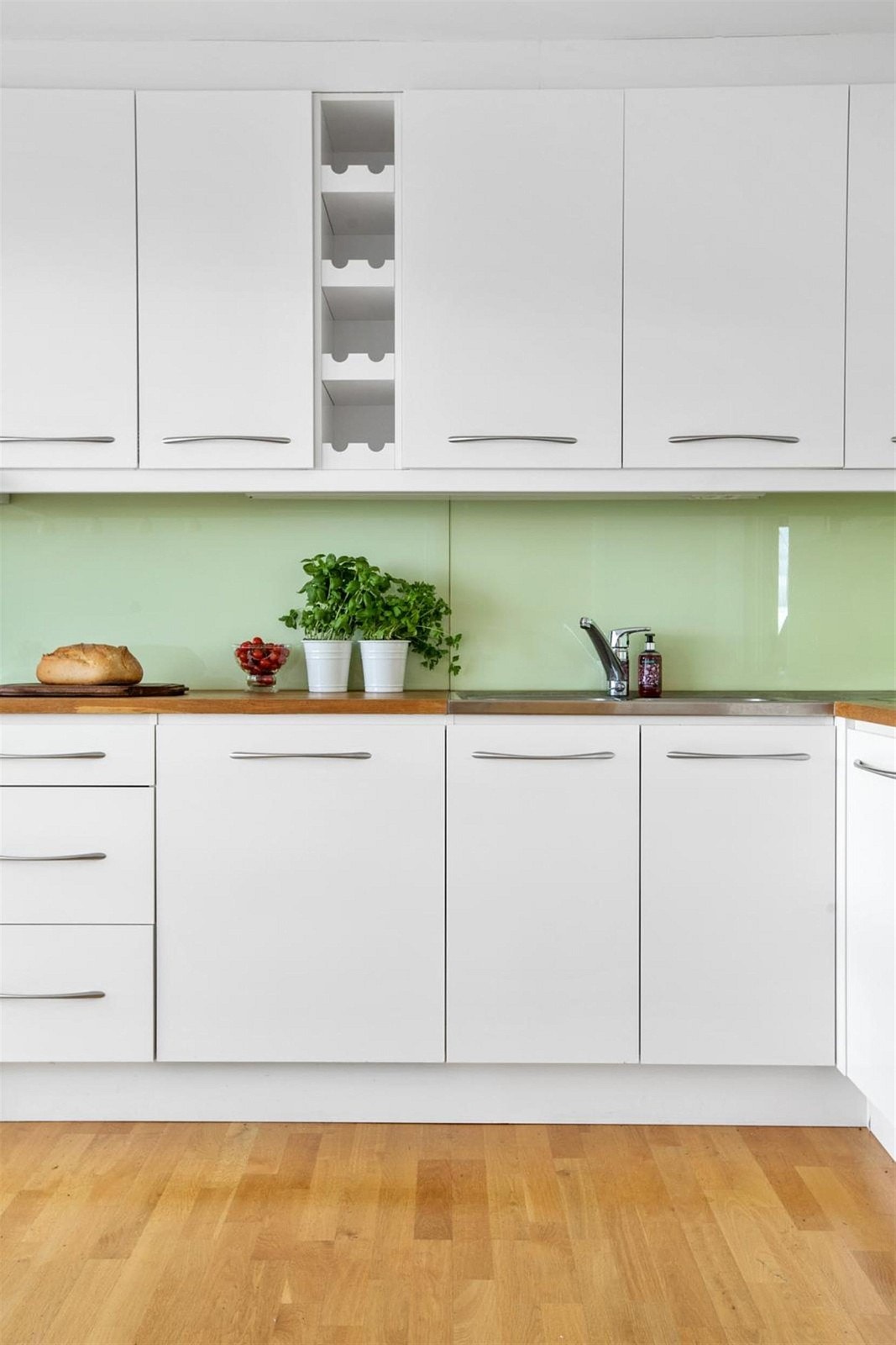 Pent og klassisk hvitt kjøkken med pen glassplate bak benk i en tidsriktig farge. Galleribilde