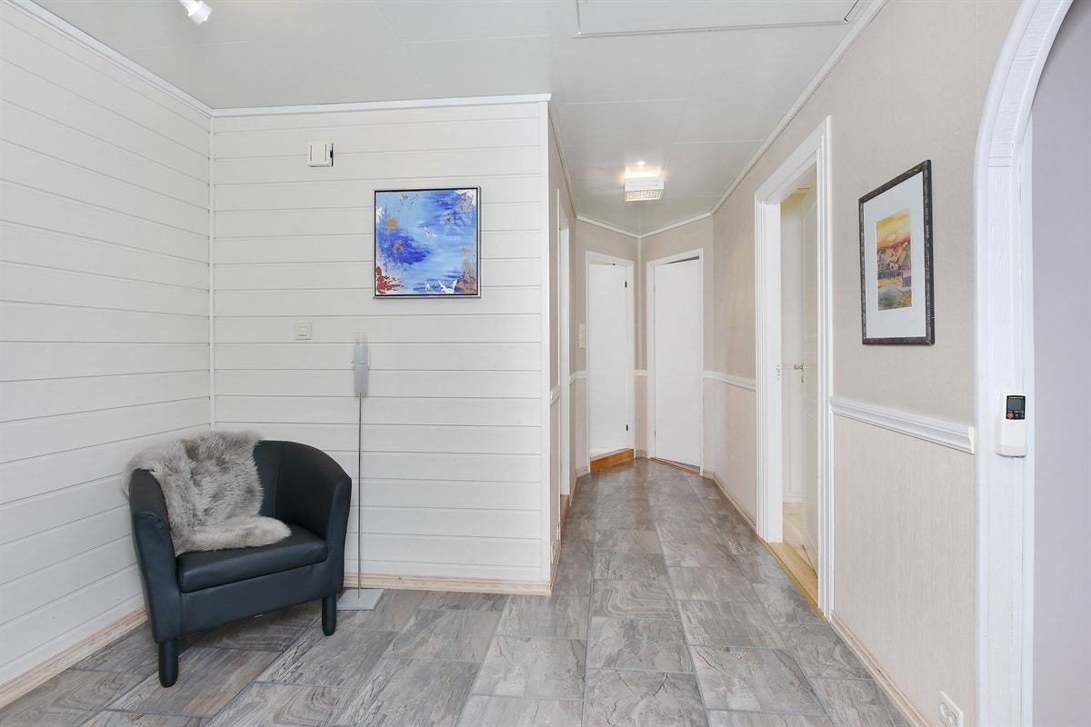 Entreen har mørk laminat på gulv, panelte overflater, et lite vindu og lysinnslipp fra glassfelt i inngangsdøren. Galleribilde