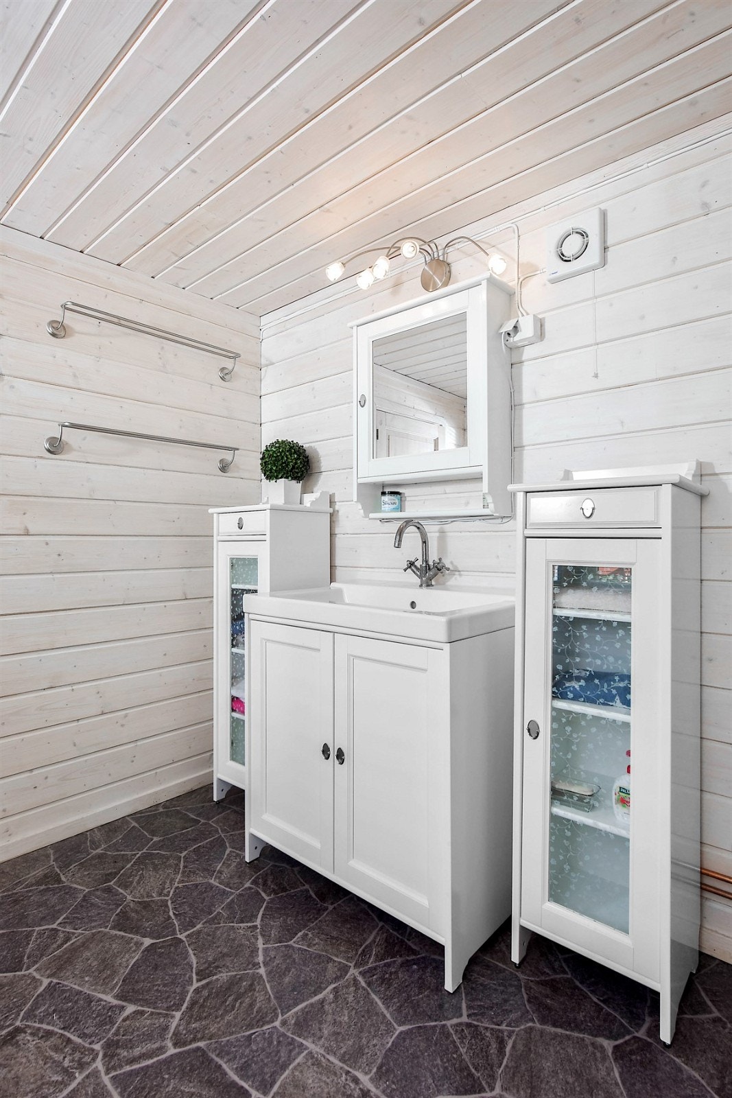 Innredningen består av heldekkende servant på koselig servantskap med lyse profilerte fronter, tilhørende speilskap, belysning og to frittstående skap med glassdører. Galleribilde