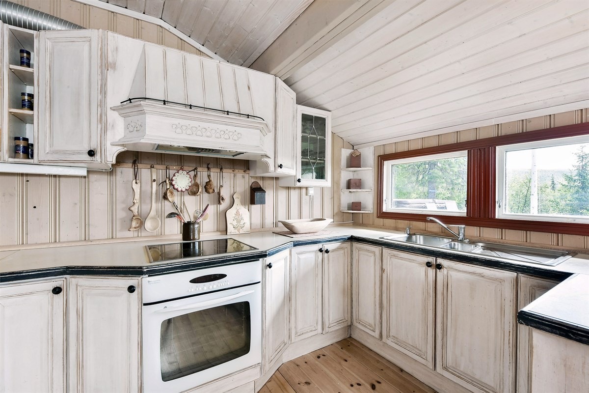 Innredningen har lyse profilerte fronter med slitte detaljer, koselige vitrineskap, vinhylle, åpne hyller og kompositt benkeplate med sort kant og oppvaskkum. Galleribilde