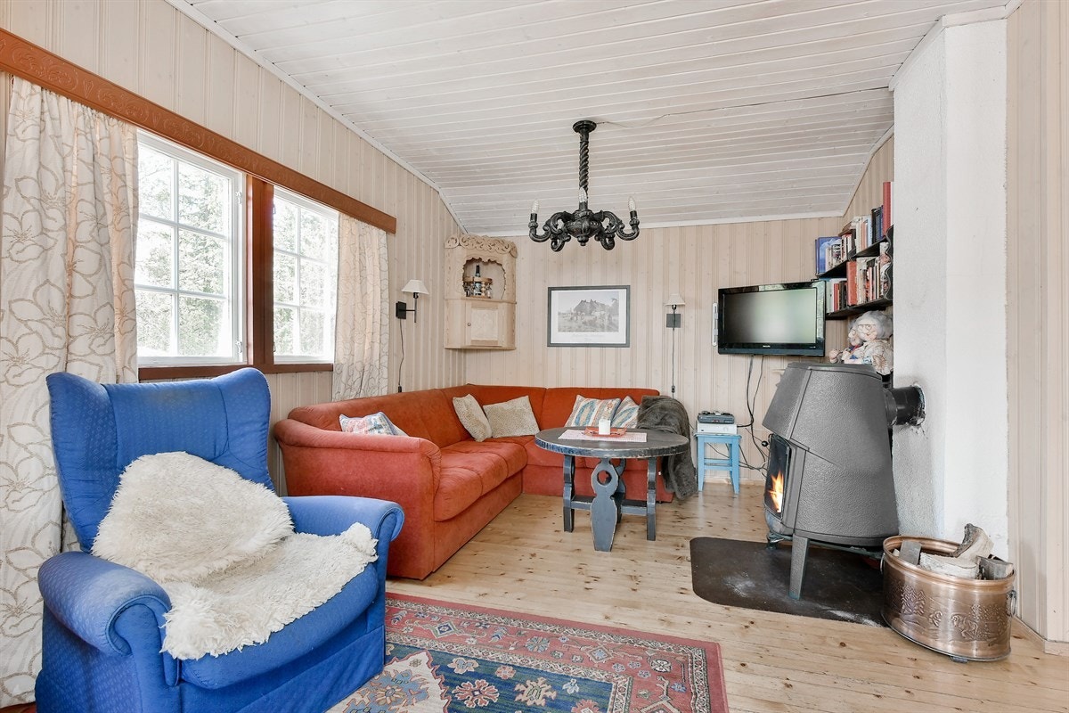 Stuen har lakkert tregulv, lysbeisede panelvegger og valmet hvitmalt tak med synlig bjelke som understreker det hele. Galleribilde