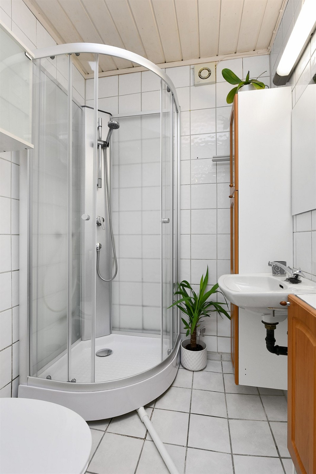 Det flislagte badet i underetasjen har gulvvarme og elektrisk avtrekksvifte. Badet er innredet med frittstående toalett, enkel servant og dusjkabinett. I tillegg har badet veggskap, høyskap og speil med belysning i overkant. Galleribilde