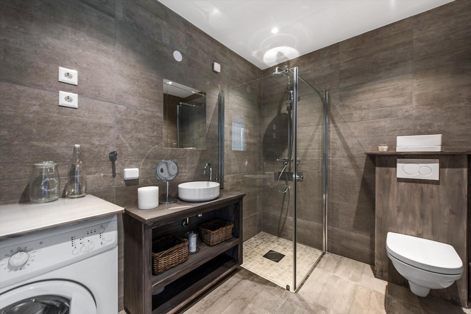 Bad i 1. etasje med gulvvarme og flislagt gulv. Dusjhjørne med innfellbare glassvegger, servant i benk uten fronter med ettgreps blandebatteri. Galleribilde