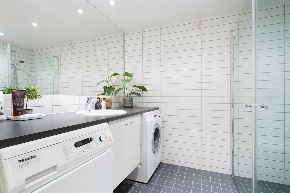 Badet ligger strategisk plassert ved entréen, og har mørke gulvfliser, hvite veggfliser og malt himling med integrert downlights Galleribilde