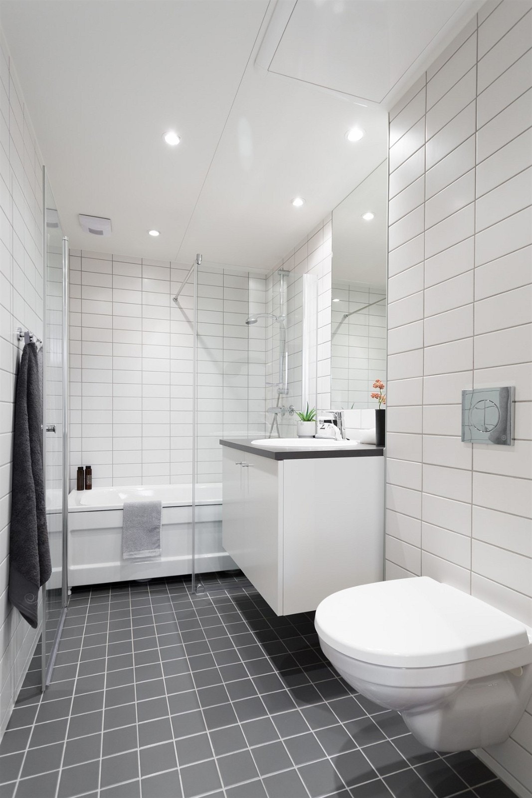 Badet fra hovedsoverom har hvite veggfliser, mørke gulvfliser med varme og malt himling med integrert downlights Galleribilde