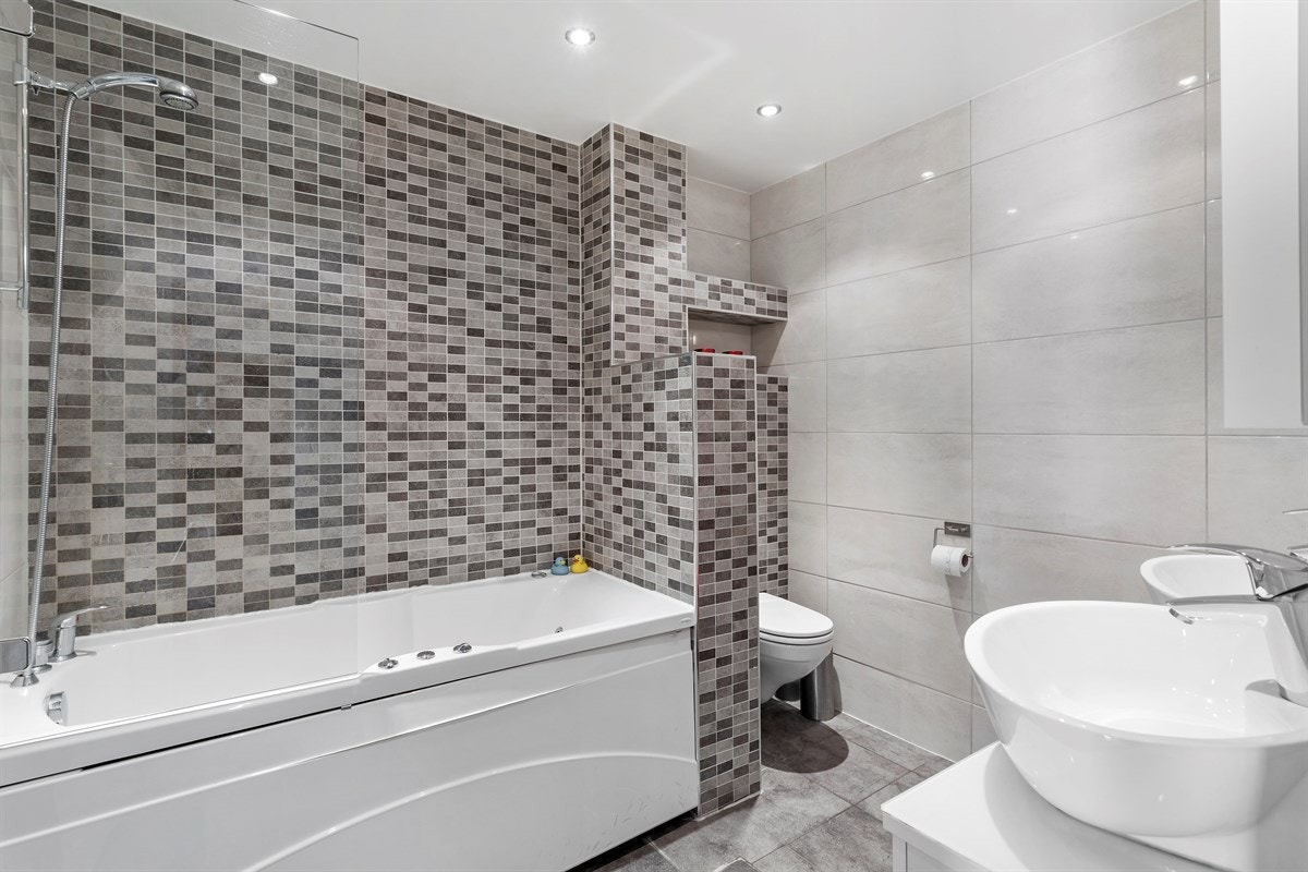 Delikat bad med massasjebadekar, wc med skjult sisterne, innredning med dobbel servant og speil. Galleribilde