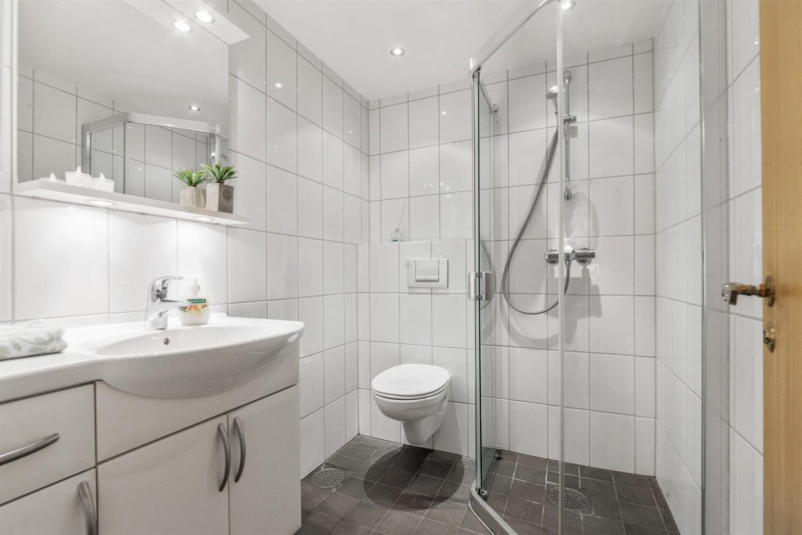 Dusjhjørne med glassdører, vegghengt toalett, nedforet himlig med dowlights Galleribilde