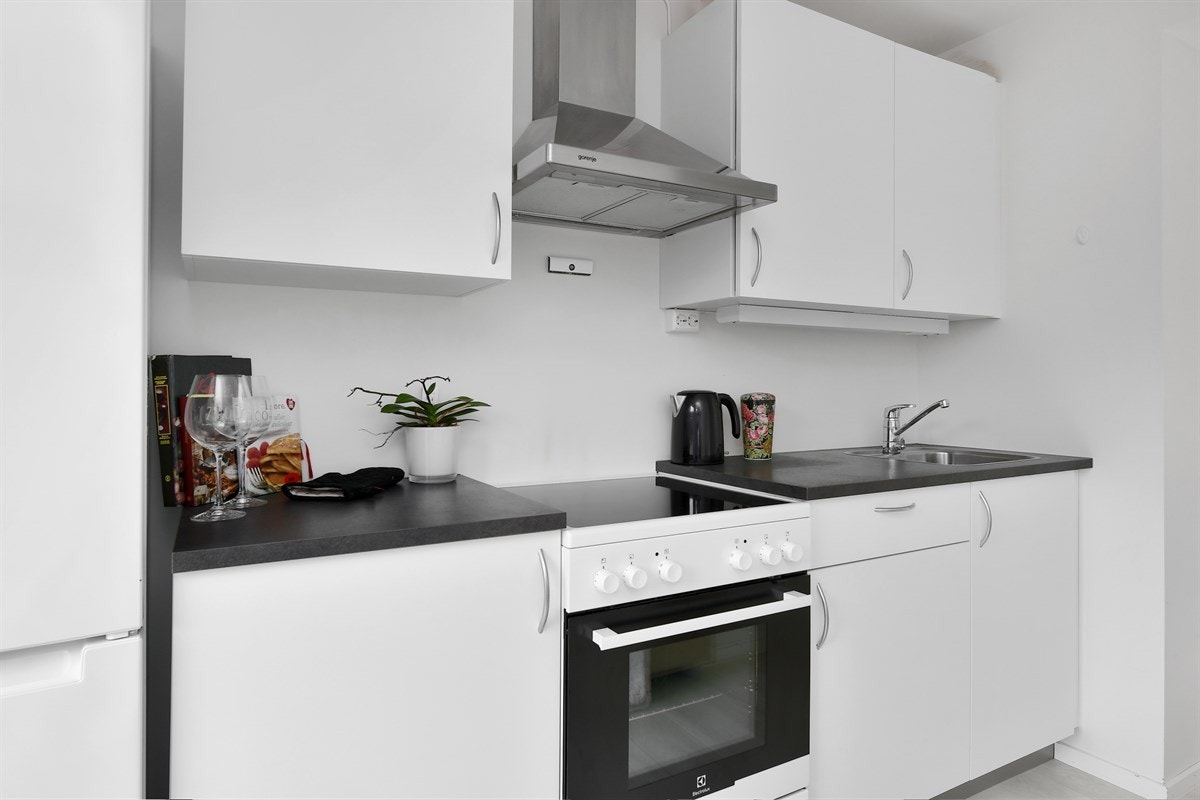 Kjøkkenet ligger langs den ene veggen og er holdt i en tidløs stil med hvite, glatte fronter, benkebelysning og laminat benkeplate med nedfelt oppvaskkum. Galleribilde