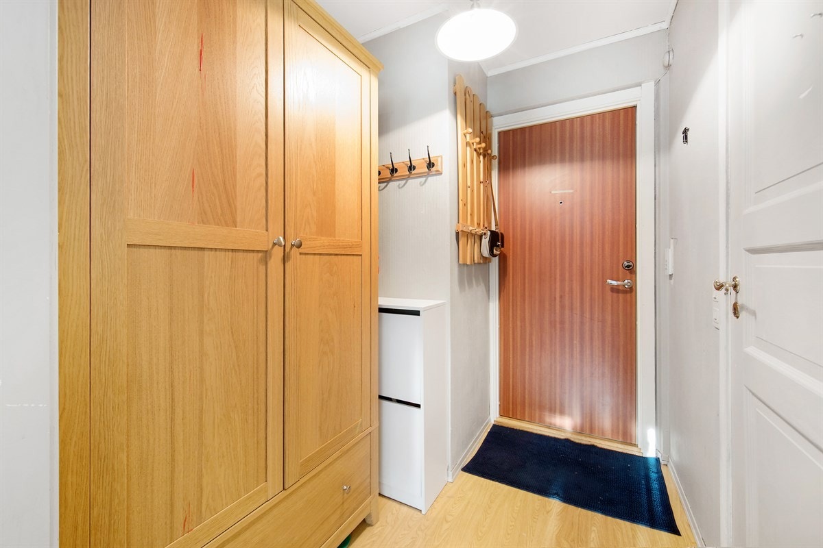 Entreen er innredet med parkettmønstret belegg på gulv og gråmalt strietapet på vegg. Galleribilde