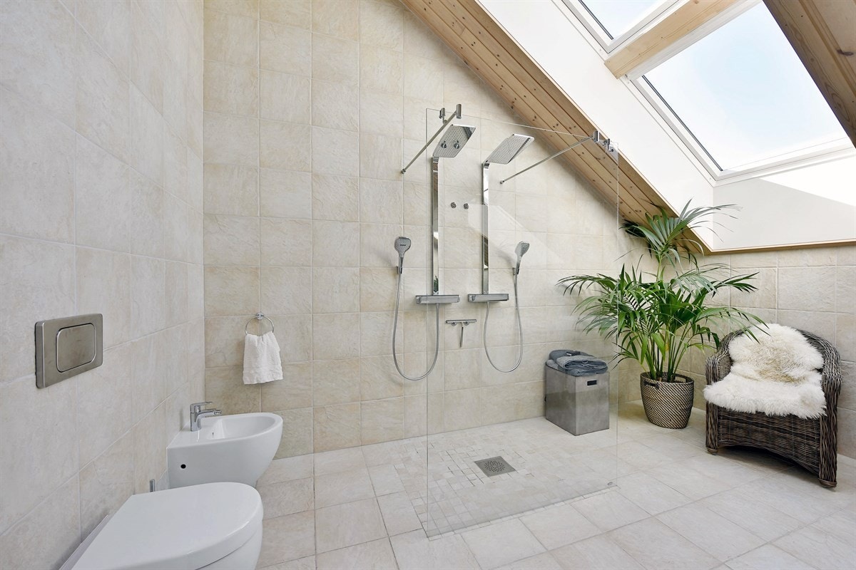 Badet i tredje etasje har store vinduer i skråtak, noe som gir rommet et delikat, luftig uttrykk. idere har badet veggmontert toalett og bidé, samt en innbydende åpen dusjløsning med to regnfallsdusjer bak glassvegg. Galleribilde