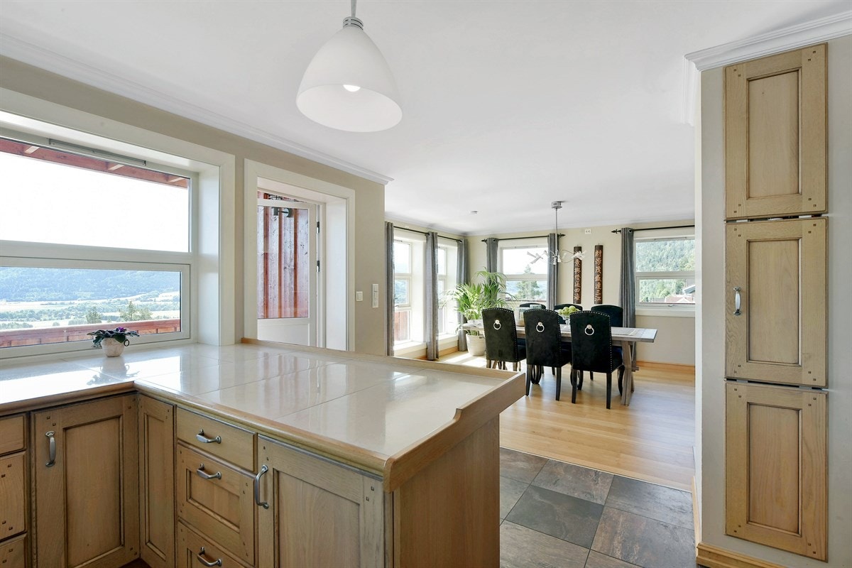 Det lyse og trivelige kjøkkenet ligger i åpen løsning mot stuens spisestuedel med mørke gulvfliser, gulvvarme, downlights i overkant av det ene vinduet, samt god skap- og benkeplass. Galleribilde