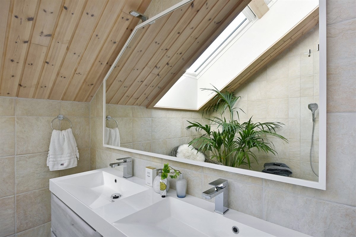 Baderomsinnredningen har lyse fronter, heldekkende dobbelservant og speil med belysning. Galleribilde