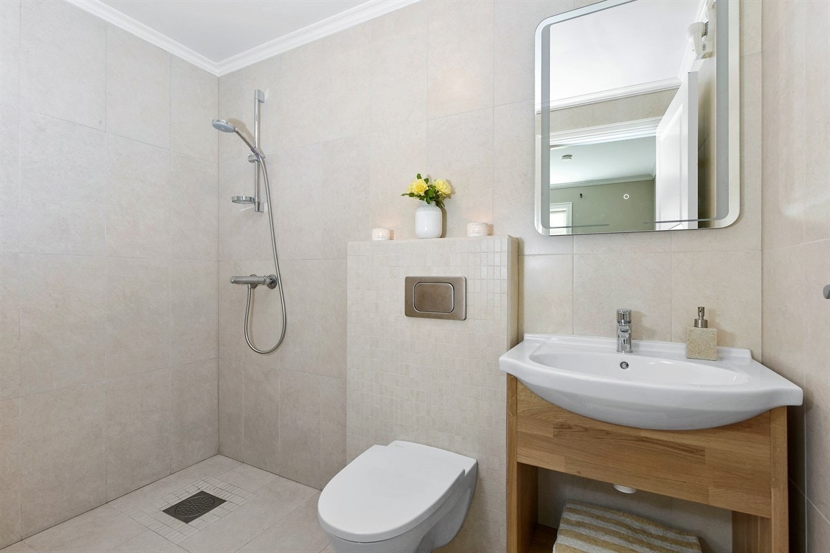 Badet i hybelen gir et delikat inntrykk med sandfargede fliser og behagelig gulvvarme. Rommet er utstyrt med veggmontert toalett, åpent dusjhjørne og opplegg for vaskemaskin. Galleribilde